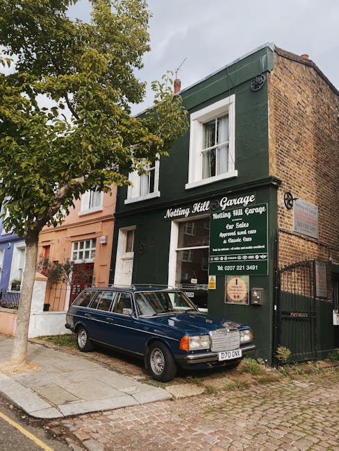 A street scene in Notting Hill with a three-storey building featuring a pink shopfront on the corner, displaying the name 'Suggaring Lane'. Several parked cars line the curb, with one vehicle partly v